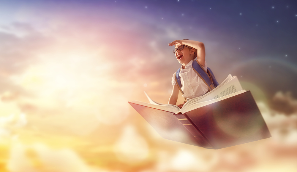 Back to school! Happy cute industrious child flying on the book on background of sunset sky. Concept of education and reading. The development of the imagination.