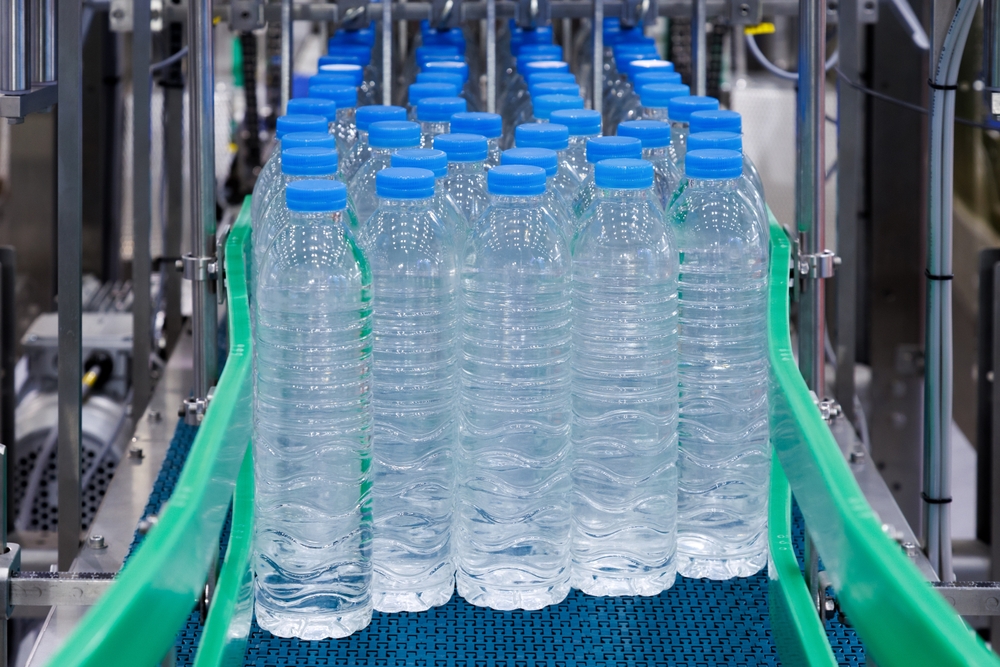 Plastic bottles with blue caps on conveyor belt in water bottling factory. Industrial production line for bottled water manufacturer.