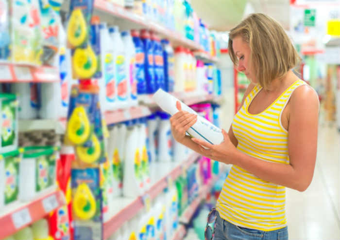Person in a supermarket reading the ingredients on a bottle of detergent