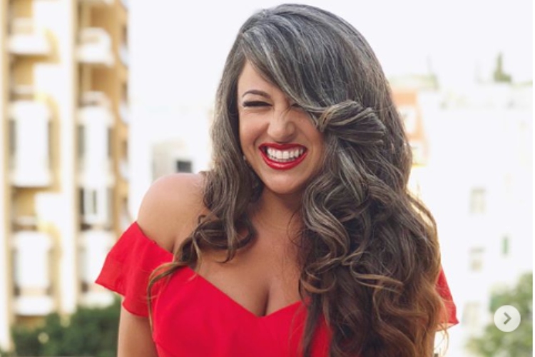 Woman in a red dress, smiling with wavy brown hair and light silver streaks