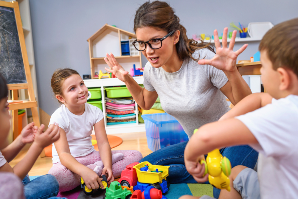 Preschool teacher talking to group of children sitting on a floor at kindergarten