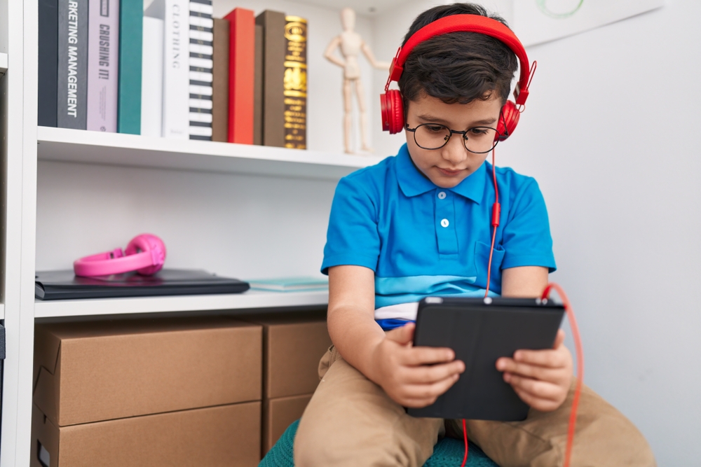 Adorable hispanic boy student watching video on touchpad at library school