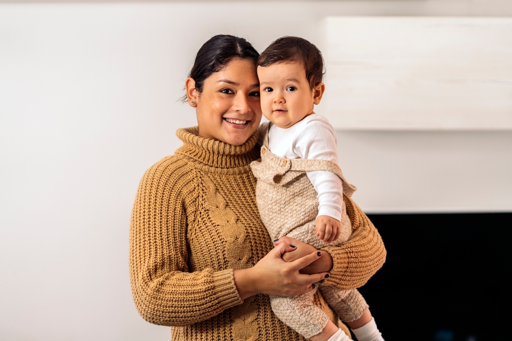 Stock photo of smiley woman holding her little baby and looking at camera.