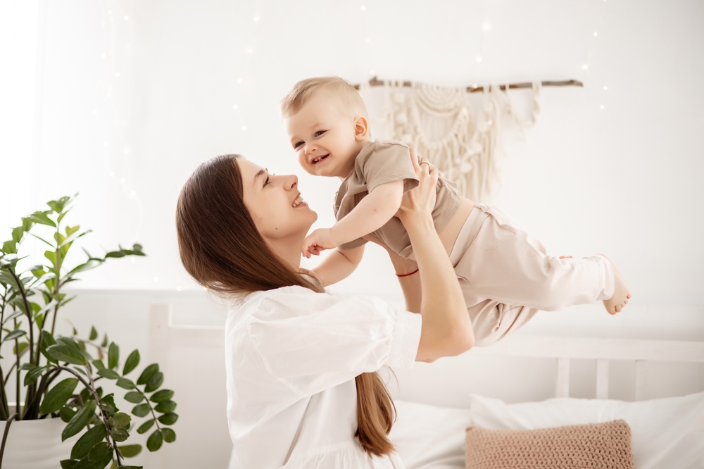 a young beautiful mother with a baby boy hugging on the bed at home in the bedroom, mother's care and love, portrait of a happy mother with a child, healthy motherhood