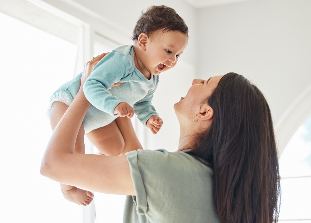 Mother holding laughing baby in home for love, care and quality time together to nurture childhood development. Happy mom, carrying and playing with infant girl kid for support, happiness and fun