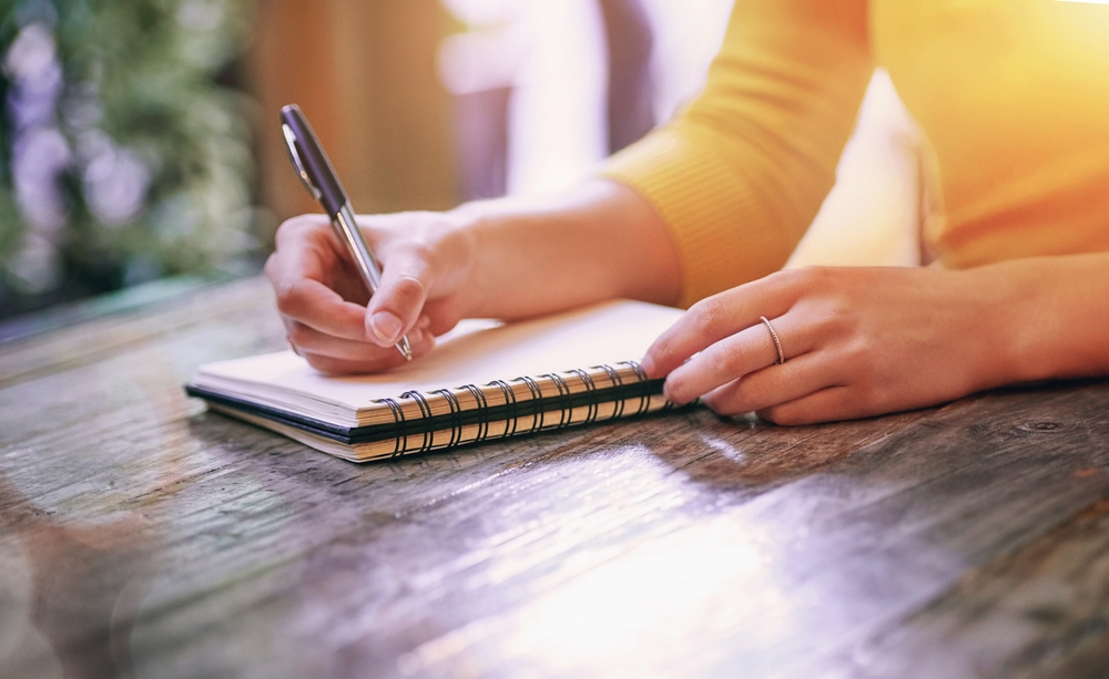 Woman, closeup and notebook for notes, schedule and planning on table in cafe with pen. Wife, writing and notepad with diary, marriage journal and letter for self care, growth and relationship goals