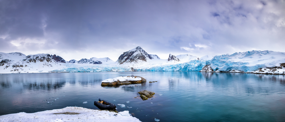 Panarama of the mountains, snow and blue glacial ice of the Smeerenburg glacier, Svalbard, and archipelago between mainland Norway and the North Pole. An inflatable boat is anchored in the foreground,
