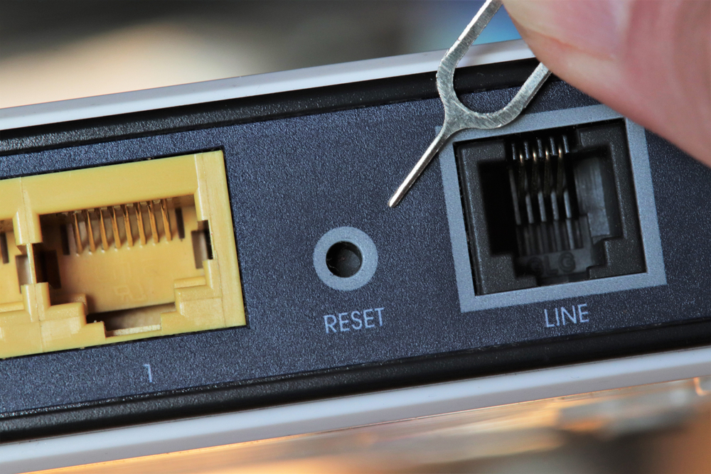 Person about the press the reset button on the back of computer hardware
