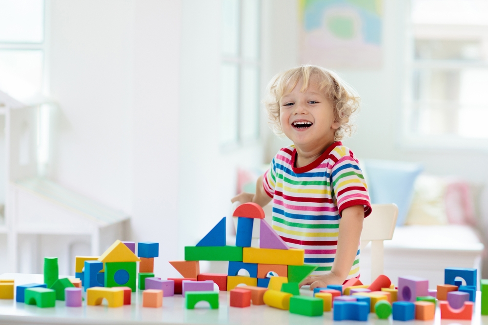 Kid playing with colorful toy blocks. Little boy building tower of block toys. Educational and creative toys and games for young children. Baby in white bedroom with rainbow bricks. Child at home.
