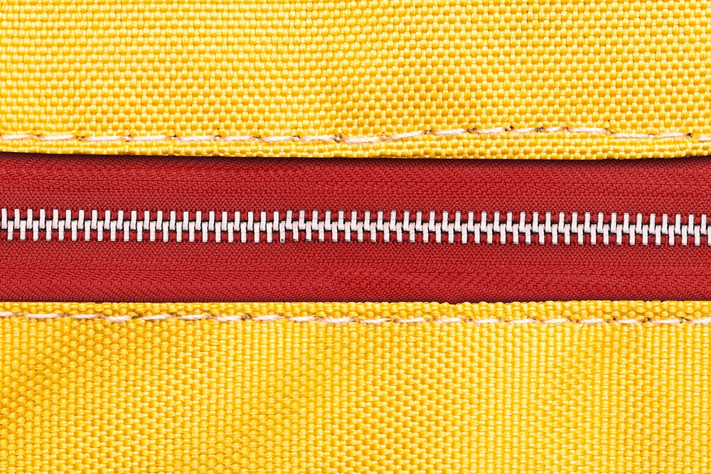 Yellow fabric red metal zipper. Vibrant color style clothing accessories. Sewer element background. Closed zipper. Zipped zipper. Silver gray shiny zipper teeth background.
