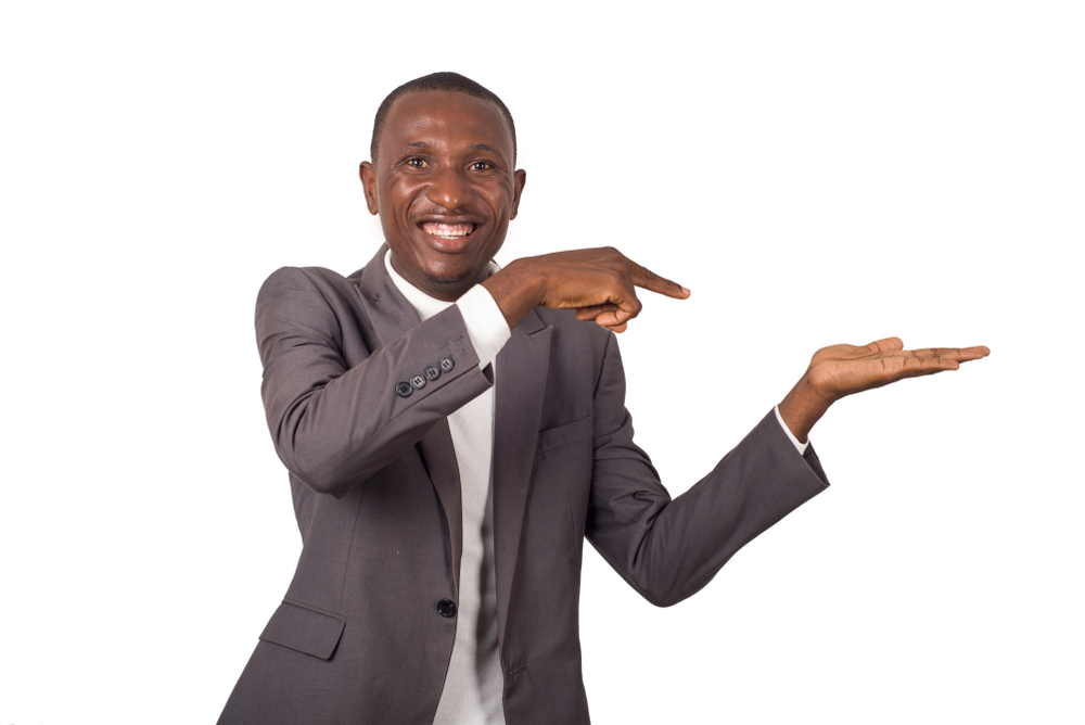 Portrait of young smiling man in suit standing on white background showing something in his left hand.