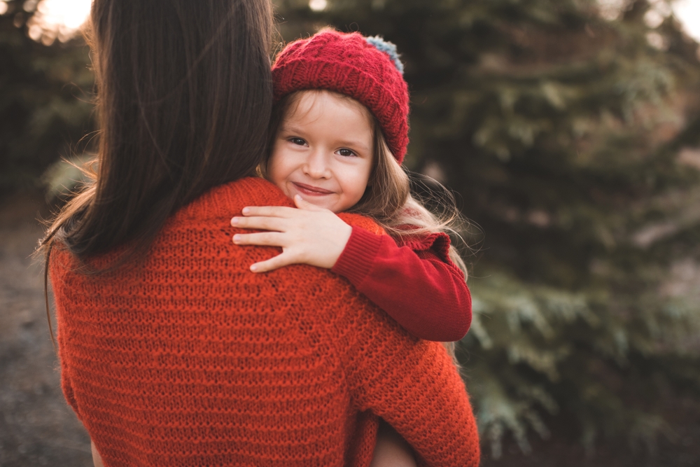 Cute smiling child girl 3-4 year old on mother hands wear knit hat and sweater outdoor. Look at camera. Christmas holiday season. Motherhood. Winter time.