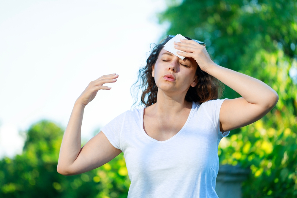 Young woman having hot flash and sweating in a warm summer day. Woman drying with paper napkin in too hot weather