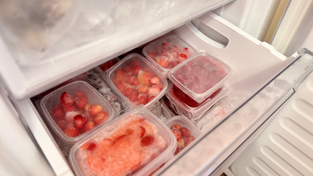 Freezer and frozen strawberries and raspberries in transparent plastic containers. Close-up