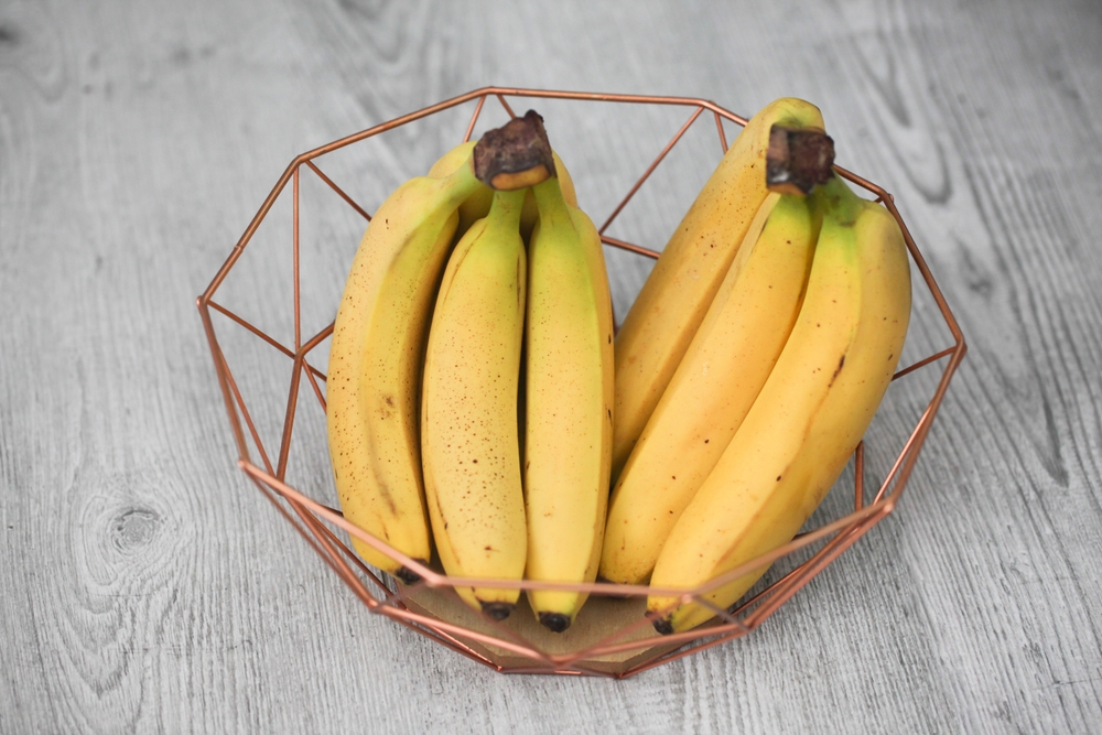 Bananas in a modern metal bowl on a grey wooden table. Stylish fruit display. Home interior design in a rustic, minimalistic kitchen setting. Bunch of bananas. Fruit background.