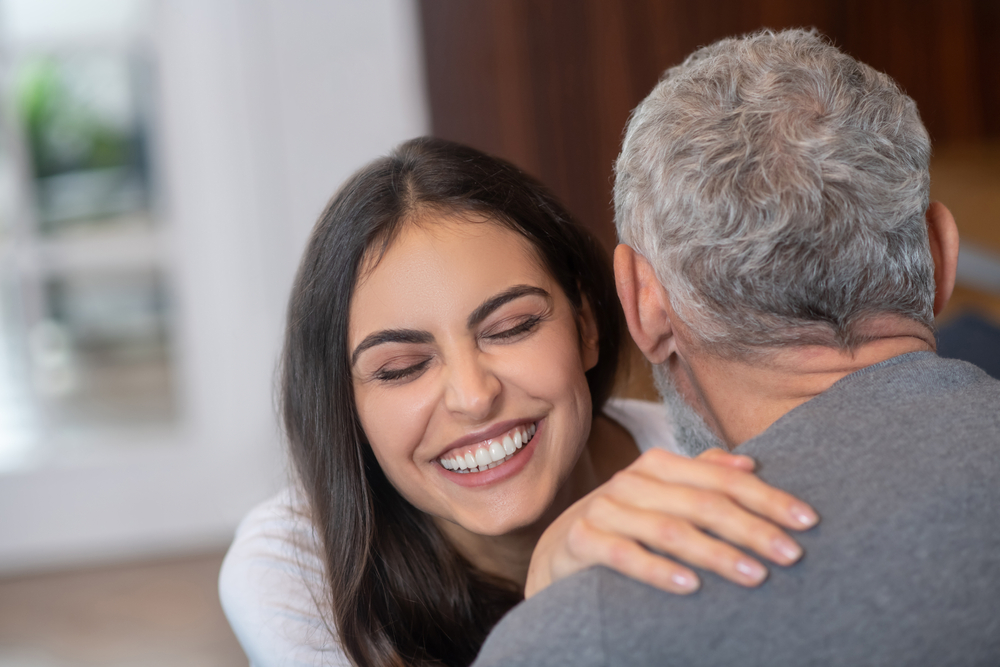 Happy relationships. A young long-haired woman hugging her grey-haired spouse