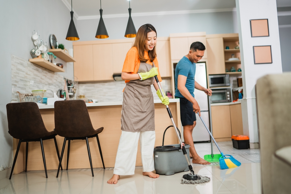 asian couple doing household chores together by mopping and sweeping the floor