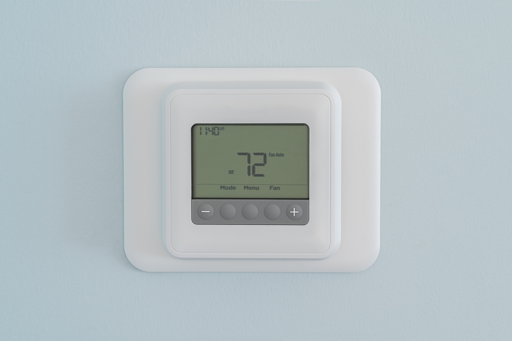 Photograph of a modern residential programmable heating and cooling thermostat set at 72 degrees mounted on a blue wall