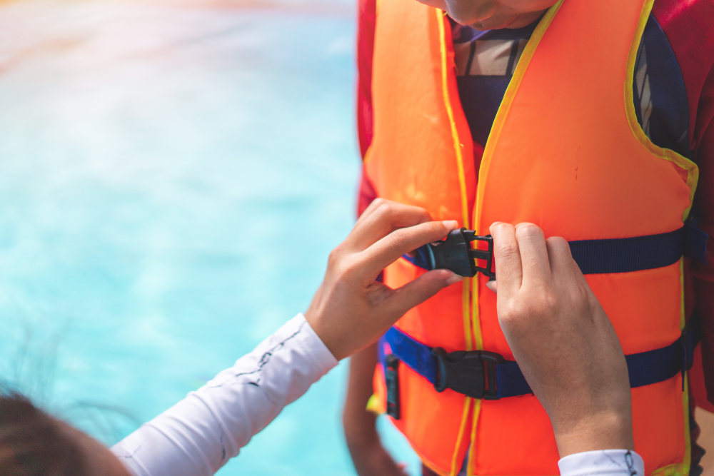 Asian mother helping her son to wear life jacket before playing in swimming pool, Selective focus.