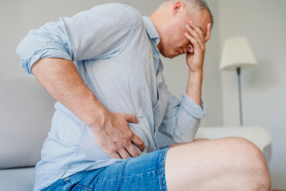 Terrible stomachache. Frustrated handsome young man hugging his belly and keeping eyes closed. Disturbed male having pain in stomach
