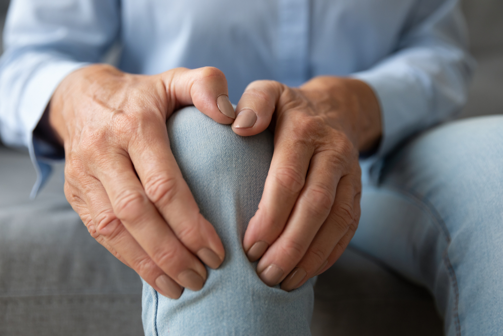 Old senior adult woman female hands touching knee sitting alone, retired elderly grandma feeling hurt joint pain in leg suffering from osteoarthritis bones disease or injury concept, close up view
