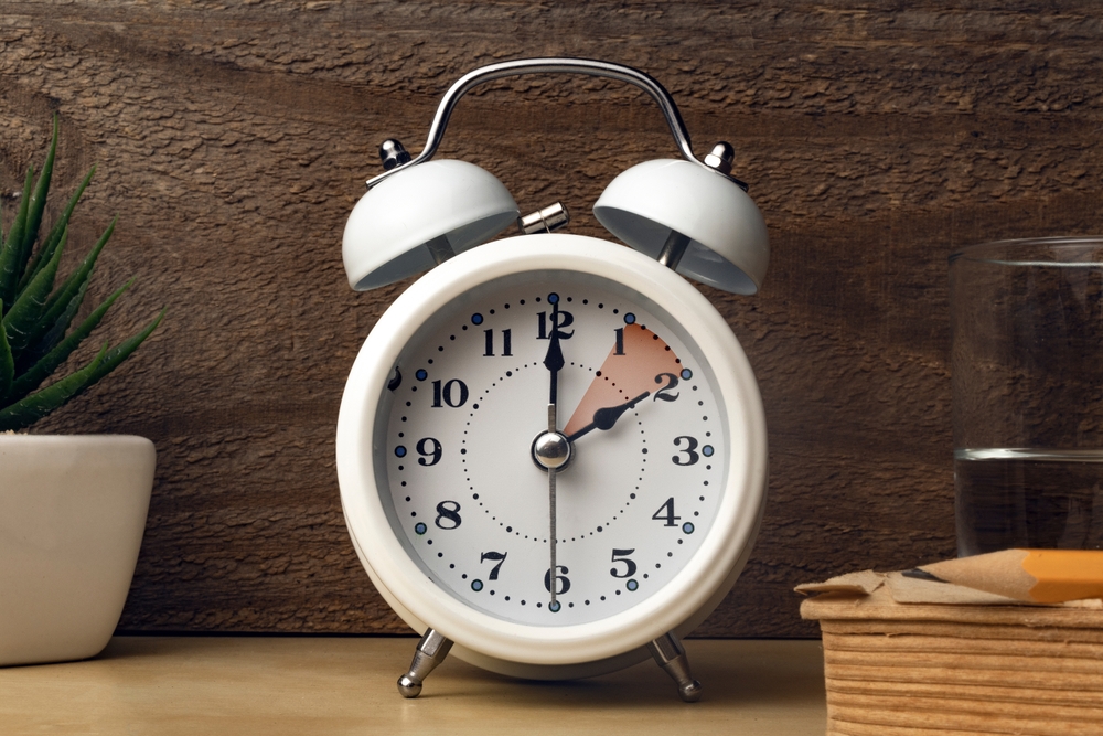 Daylight saving time concept: an alarm clock placed on a bedside table with an indication to move the hands backward
