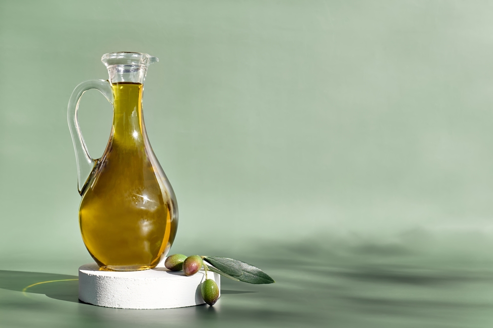 Extra virgin olive oil and olive branch in the bottle on white podium on light green background. Healthy mediterranean food.
