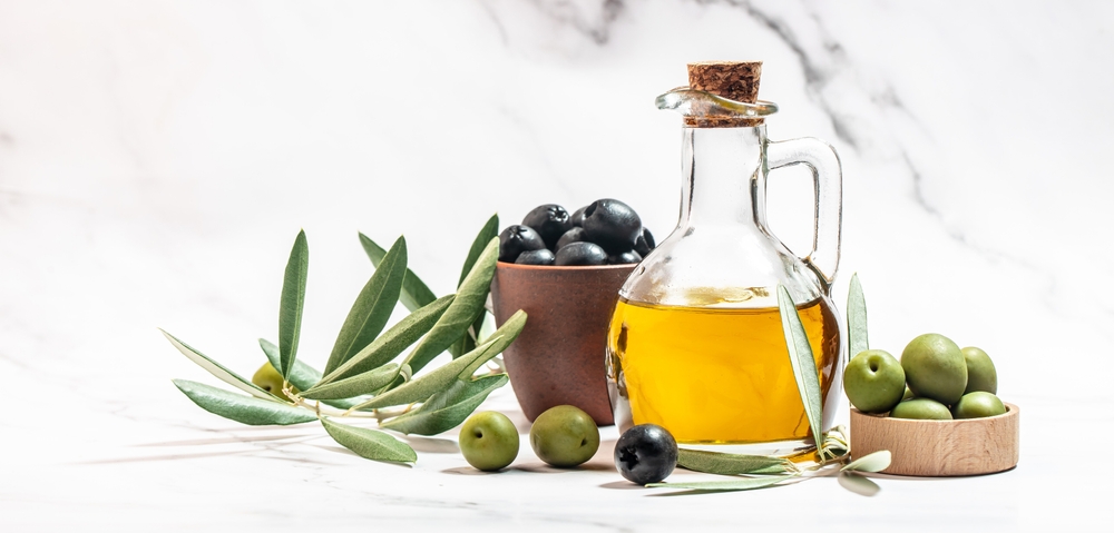 Olive oil in two glass containers and harvest olives berries in bowls on a light background. Long banner format.
