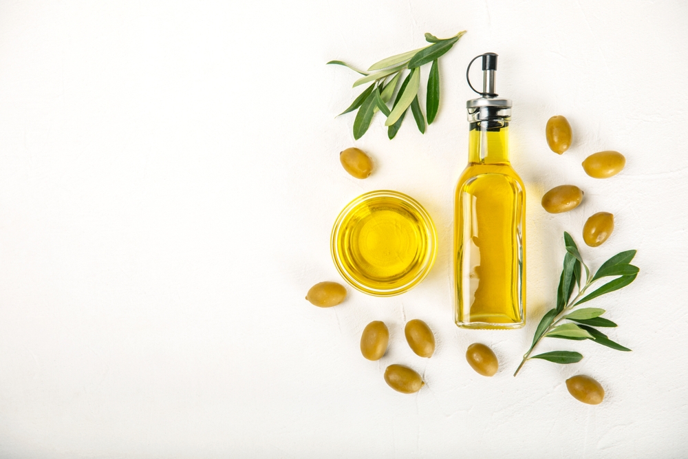 Olive oil in a bottle on a white texture background. Oil bottle with branches and fruits of olives. Place for text. copy space. cooking oil and salad dressing.

