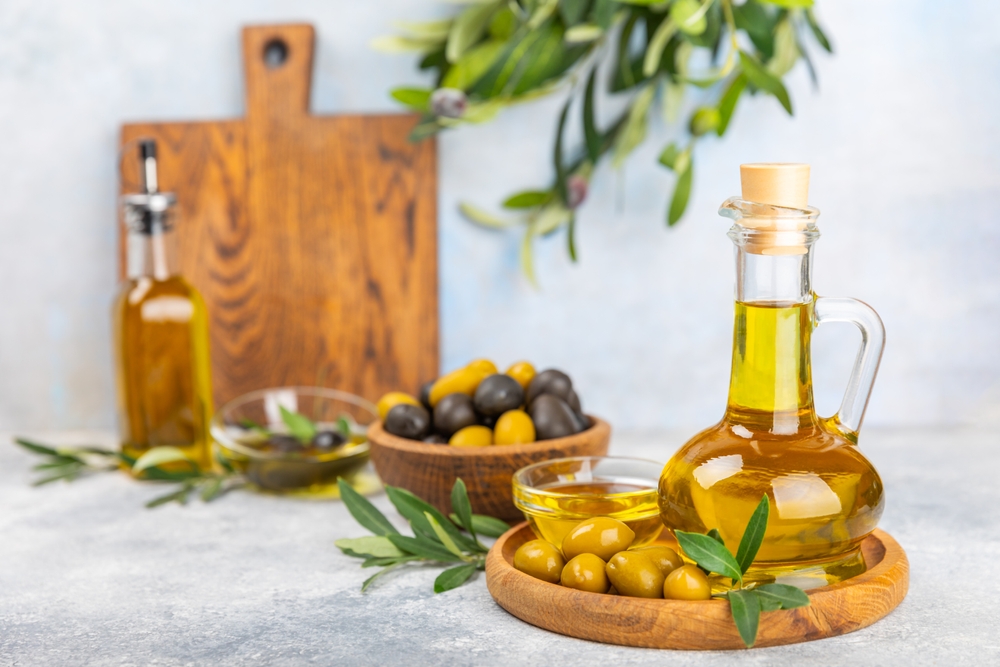 Olive oil in a bottle and gravy boat on the kitchen table. Oil bottle with branches and fruits of olives. Place for text. copy space. vegetable oil and salad dressing.
