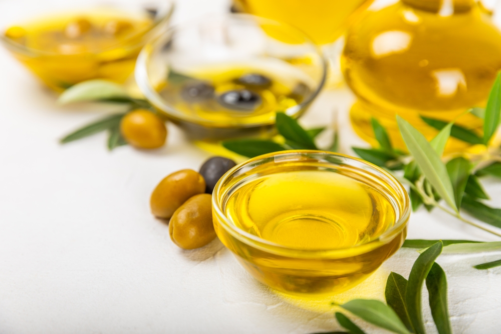 Olive oil in a bottle on a white texture background. Oil bottle with branches and fruits of olives. Place for text. copy space. cooking oil and salad dressing.
