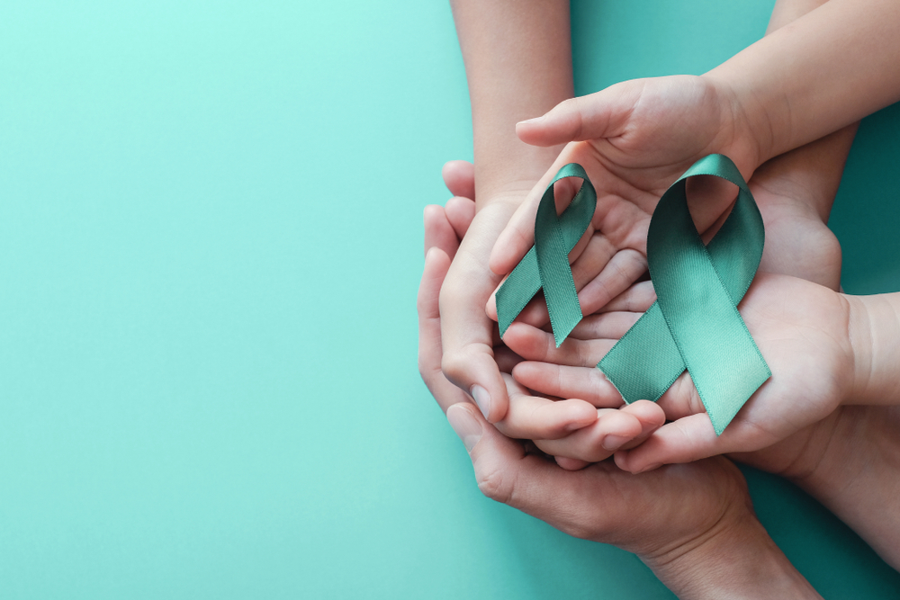 hands holding Teal ribbons on blue background, Ovarian Cancer, cervical Cancer, PCOS, anti bullying and sexual assault awareness