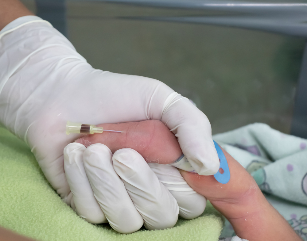 Nurse´s hand with gloves making blood test by venipuncture from newborn baby patient at the nursery in hospital