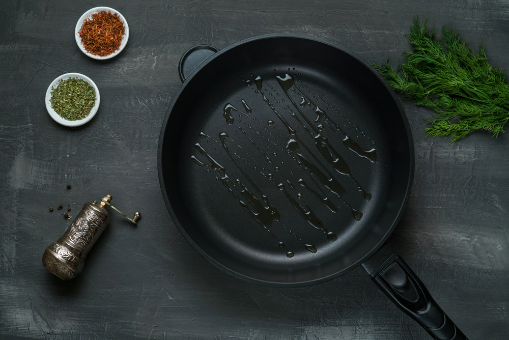 Man pouring cooking oil on the frying pan - Top View on a dark background