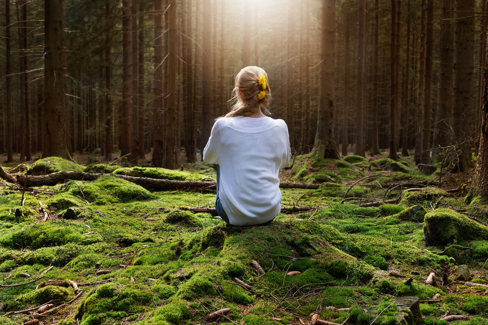 Woman sitting in forest enjoys the silence and beauty of nature.