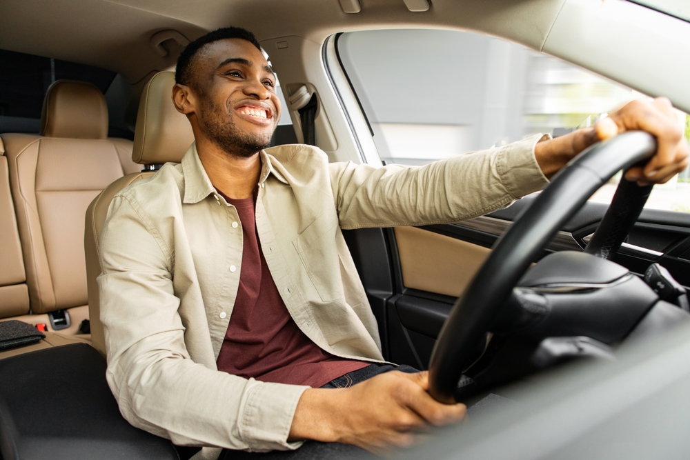 Portrait of happy african american man driving car with beige interior