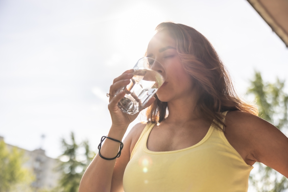 Dehydrated woman drinks clean water from a glass to replenish fluids during hot summer days.
