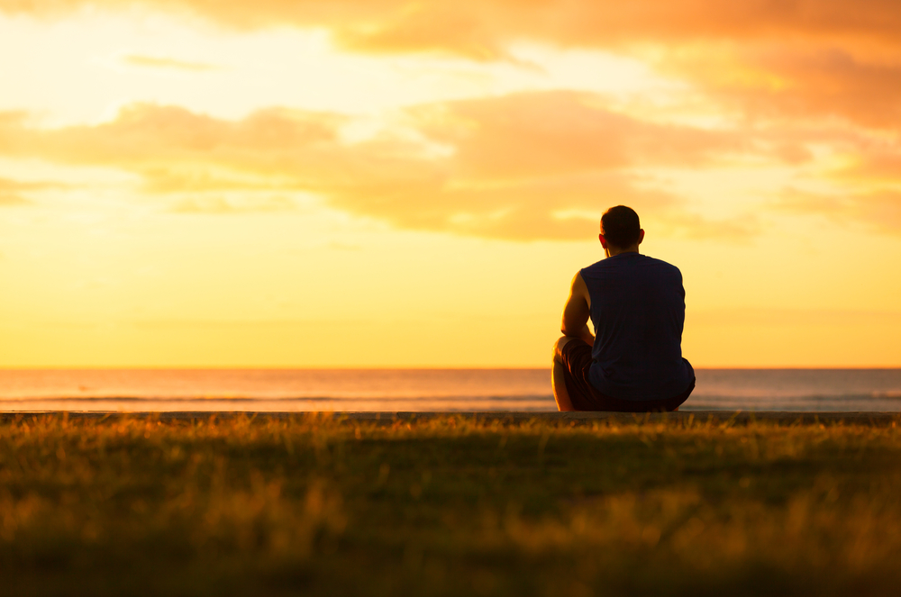 Young man sitting outdoors watching the sunset. Thinking and relaxing concept.