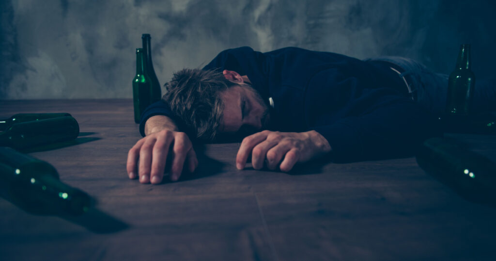 Low angle close up view photo portrait of tired exhausted unconscious guy lying sleeping on floor surrounded by empty bottles