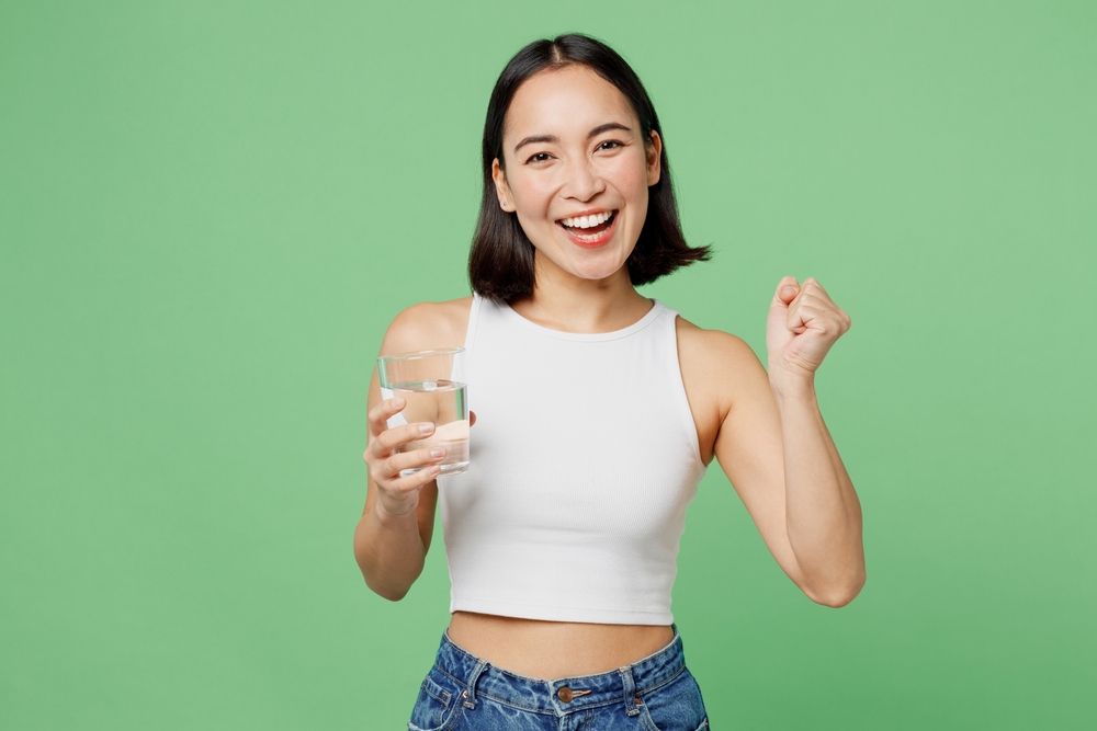 Young woman wear white clothes hold drink clear fresh pure still water from glass do winner gesture isolated on plain pastel light green background. Proper nutrition healthy fast food choice concept