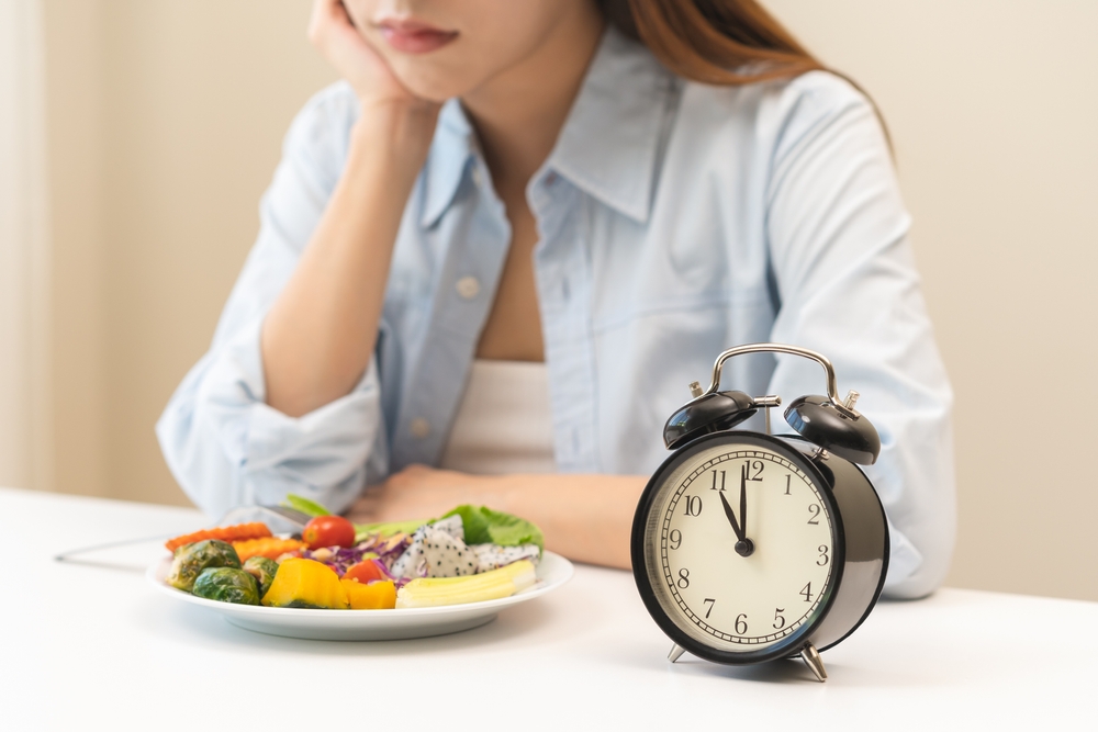 Intermittent fasting with clock, close up young woman, girl diet, waiting time to eat ketogenic low carb, green vegetable salad on plate. Eat food healthy first meal on brunch, lunch on table at home.
