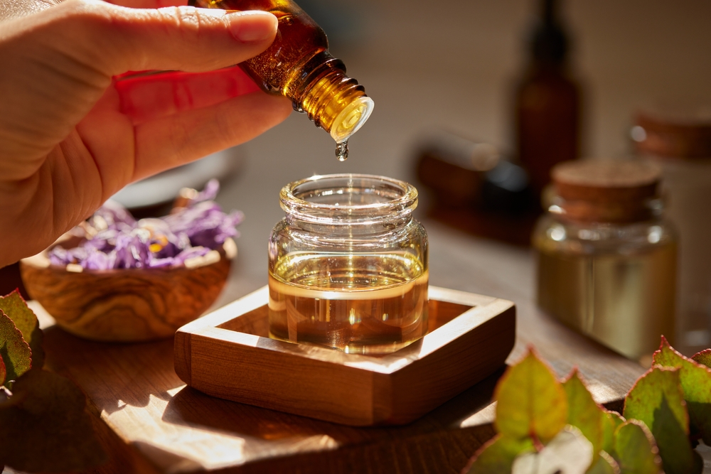 Preparing massage oil dropping essential oil. Woman dripping aromatic essential oil for a spa beauty treatment into a bigger jar. Organic oil for aromatherapy being prepared with herbs and flowers.