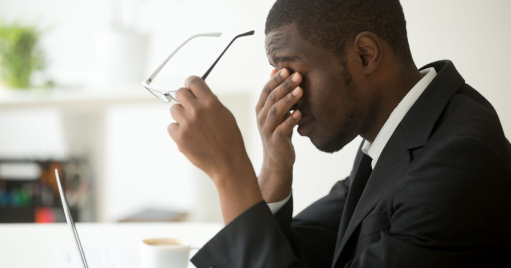 Tired of computer african businessman taking off glasses feels eye strain fatigue after long office work on laptop, exhausted overworked stressed depressed black man having bad sight vision problem