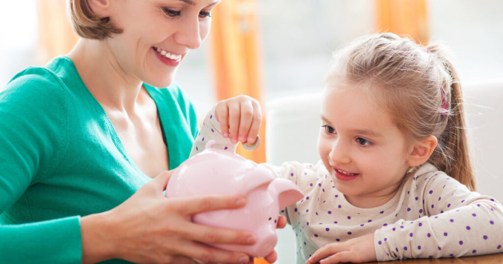 Mother and daughter putting coins into piggy bank