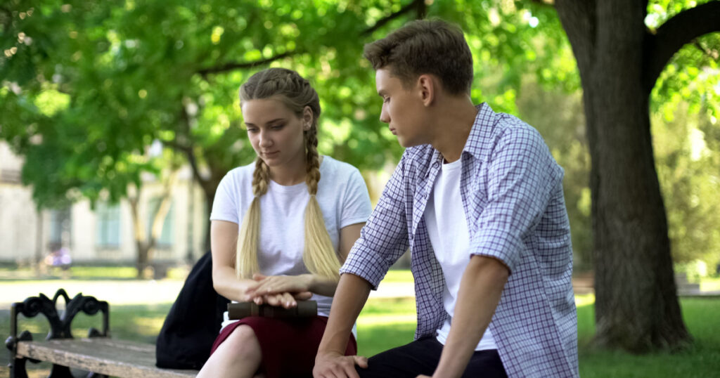 teenage girl and boy on bench lookign upset