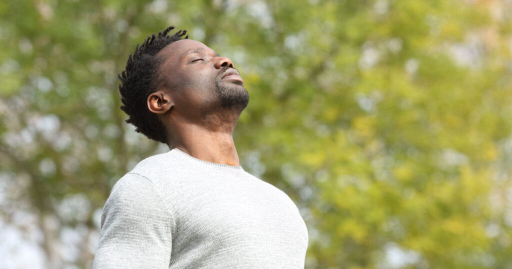 man breathing deeply fresh air in a park a sunny day with a green tree in the background