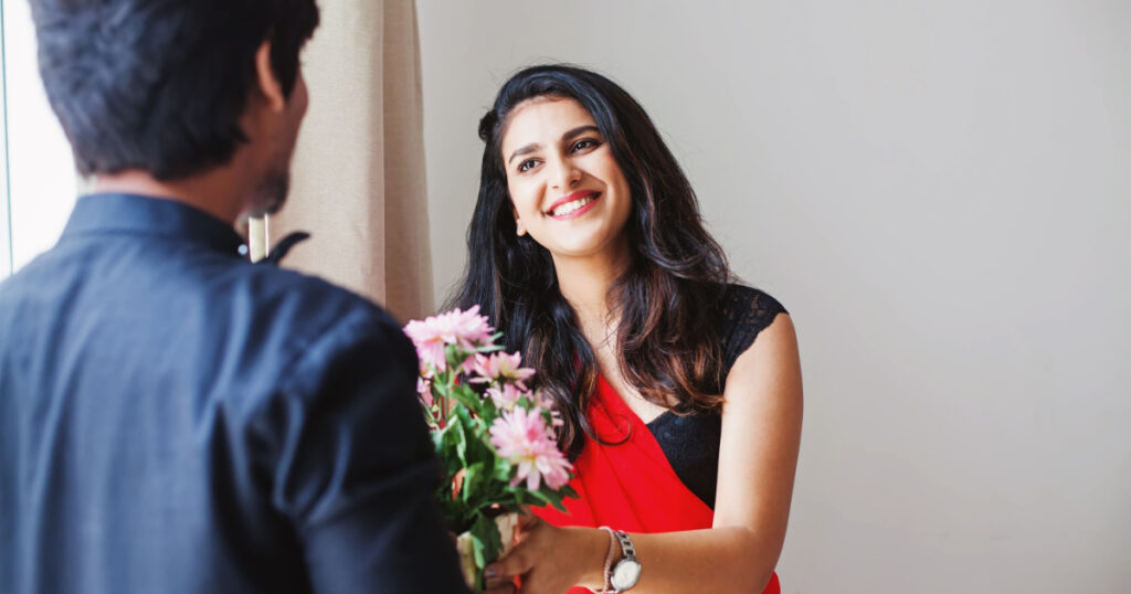 Happy Indian woman in saree receiving flowers from the man visiting for celebration