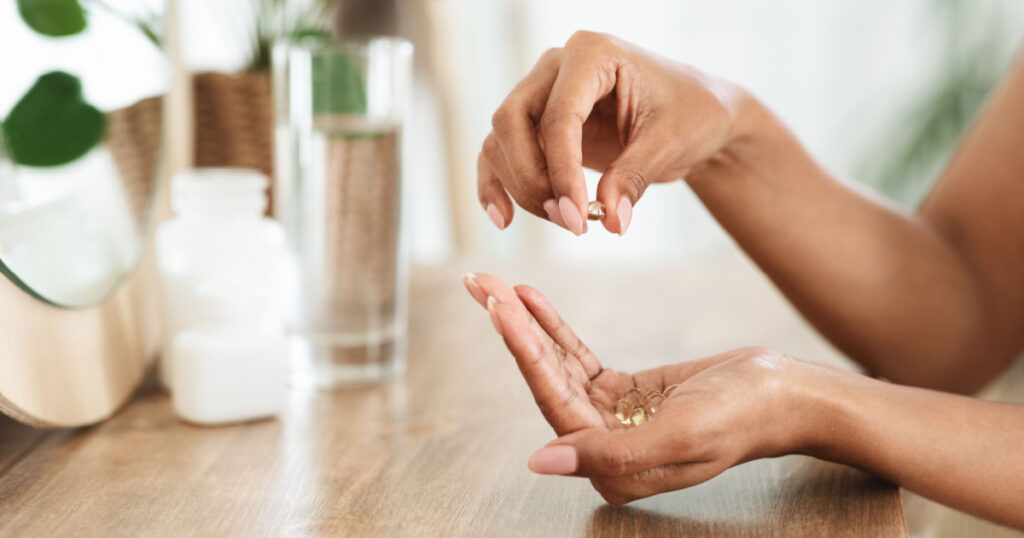 Unrecognizable African Woman Taking Beauty Supplements For Glowing Skin, Holding Omega-3 Fish Oil Capsules In Hands, Side View