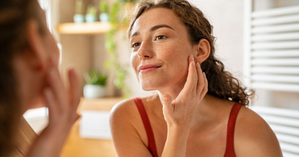girl looking at mirror while touching her face