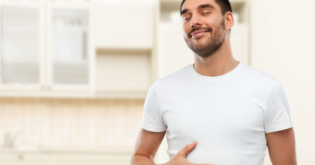 eating, satisfaction and people concept - happy full man touching his tummy over kitchen background
